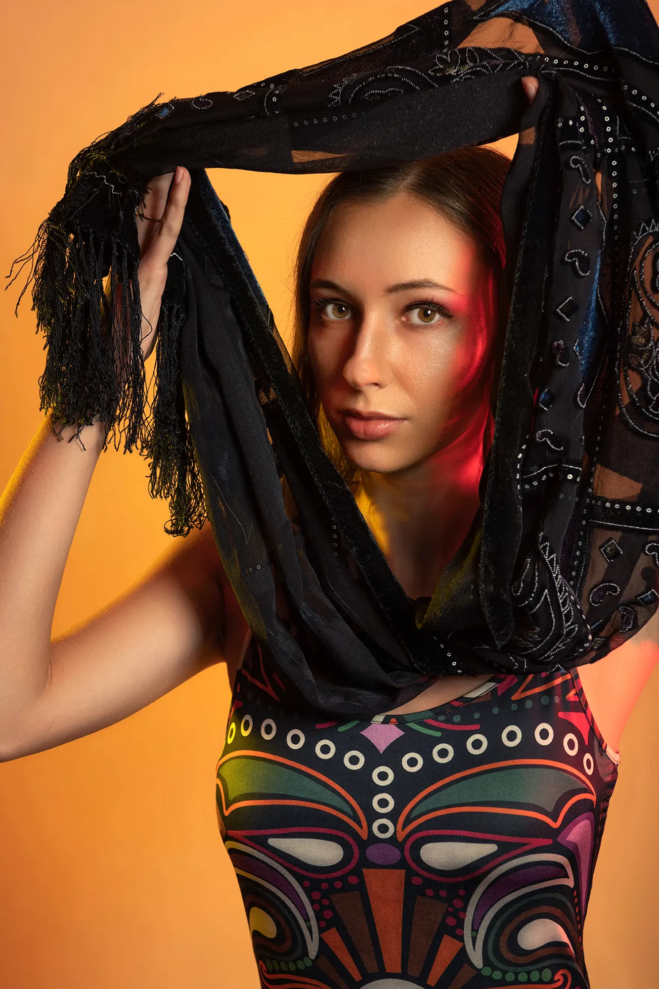 Young woman in colorful patterned dress with black fringe scarf, warm yellow background, vibrant fashion