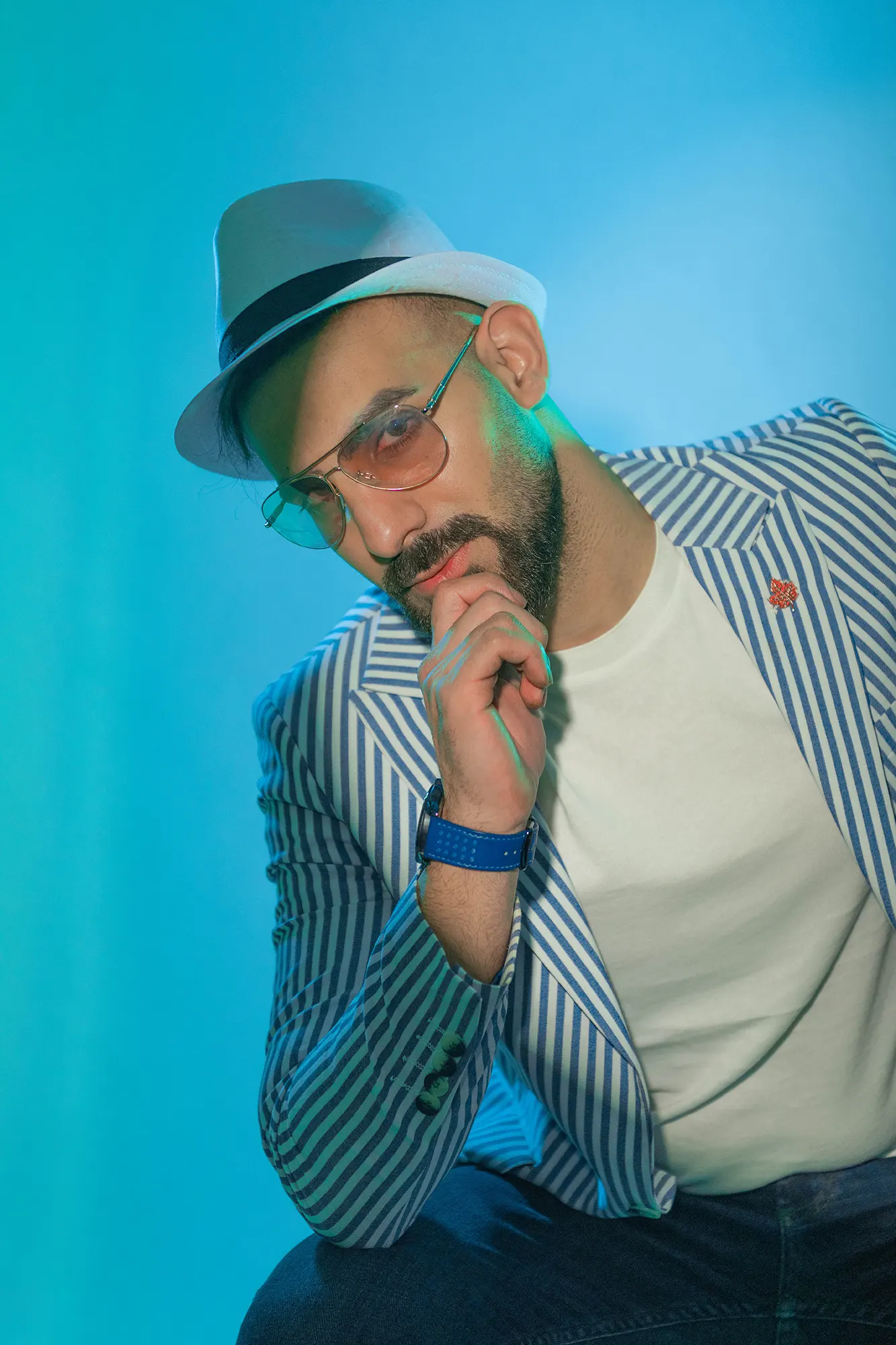 Stylish man in fedora, striped blazer, and sunglasses, with a thoughtful expression.
