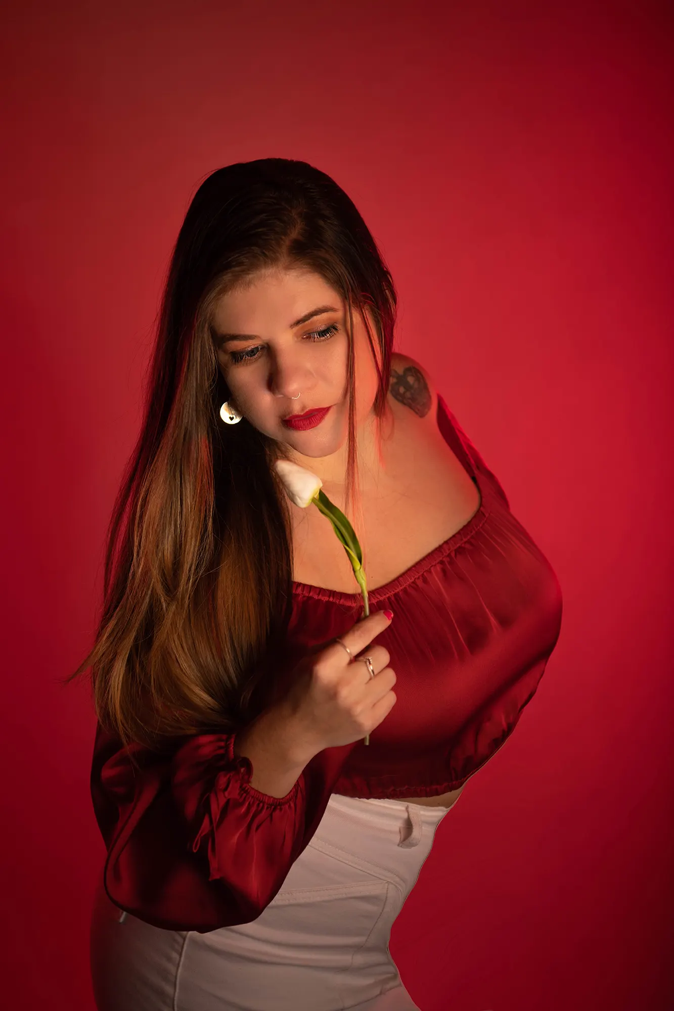 Young woman with long brown hair posing elegantly with a white tulip against a red background