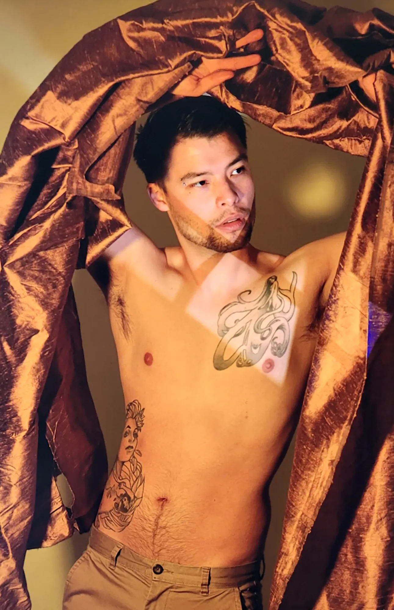 Masculine person with artistic tattoos and bronze fabric showing professional posing techniques