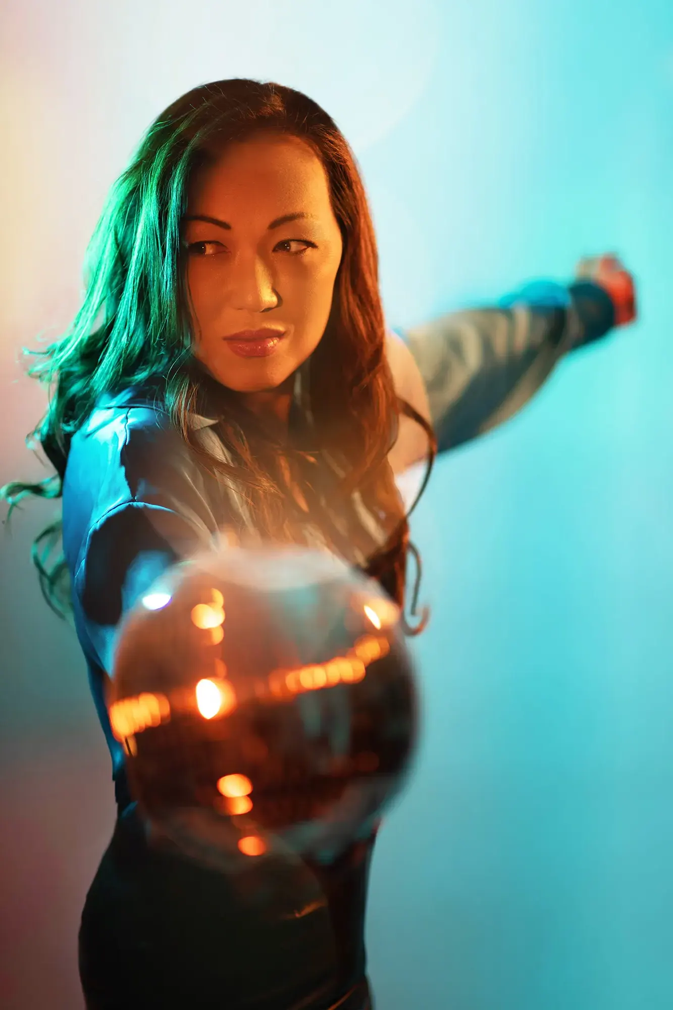 Confident Asian woman in teal shirt holding glowing orb, displaying how to interact with props for a professional UGC look.